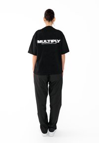 Černé bavlněné tričko s volným střihem, na zadní straně s bílým potiskem textu "MULTIPLY APPAREL CLUB." Vybaveno s černými kalhotami.