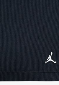 Tamsiai mėlynas grublėtas audinys su baltu Jumpman logotipu apatinėje kampe. Audinio tekstūra yra minkšta, su šiek tiek elastingumo, teikianti komfortą.