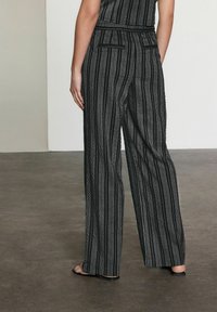 Pantalone širokog kroja s crno-bijelim prugama od teksturirane tkanine, s dva stražnja džepa i krojenom strukom. Glatke ravne sandale.