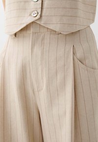 Beige op maat gemaakte broek met subtiele roze verticale strepen, gemaakt van een gestructureerde stof. Beschikt over een zijzak en een ontspannen pasvorm ontwerp.