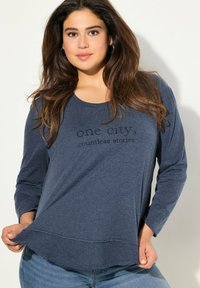 Dunkelblaues Langarmshirt mit einem runden Ausschnitt und abgerundetem Saum. Mit dem aufgestempelten Text "eine Stadt, unzählige Geschichten".
