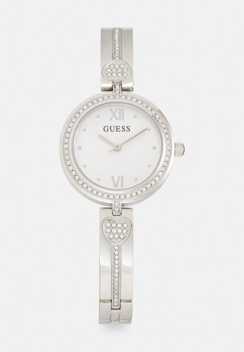 Silver Guess-klocka med rund urtavla, vit urtavla, romerska siffror och kristallprydnader. Har en hjärtformad dekoration på armbandet.