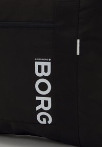 Saco de tecido preto com um grande logótipo branco "BORG". Inclui um bolso com fecho éclair e uma pega robusta para fácil transporte.
