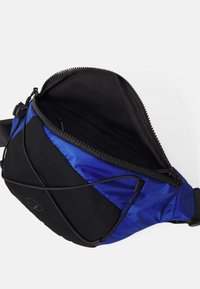 Blaues und schwarzes Umhängetasche mit einem Reißverschluss, einer strukturierten Außenseite und einer Innentasche. Verstellbarer Riemen und elastisches Schnurdetaill.