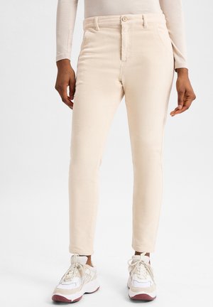 Beige Cord-Hosen mit schmaler Passform, ausgestattet mit einem Knopfverschluss, Vorderseitentaschen und strukturiertem Stoff, kombiniert mit weißen und beigen Sneakers.