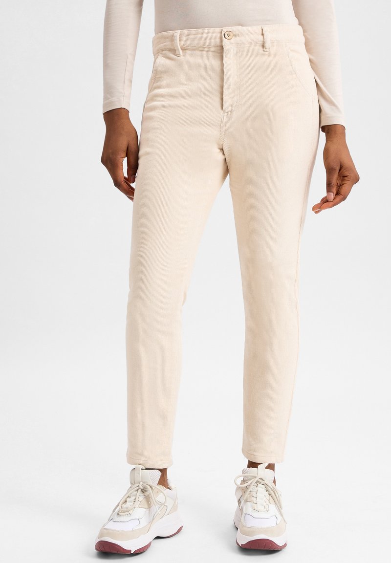 Beige ribfluwelen broek met een slim fit, voorzien van een knoopsluiting, voorzakken en een gestructureerde stof, gecombineerd met witte en beige sneakers.
