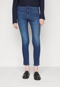 Jeans aderenti in denim blu medio, con design a cinque tasche, leggero effetto invecchiato e orlo sfrangiato. Abbinate a mocassini neri.