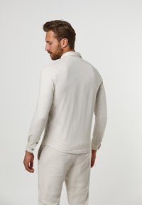 Light gray long-sleeve shirt with a buttoned collar, smooth texture, and a relaxed fit. Features button accents on the cuffs.