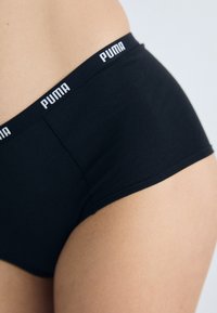 Čierne elastické bavlnené hipster nohavičky s širokým elastickým pásom s bielym logom "PUMA". Hladká textúra a priliehavý design.