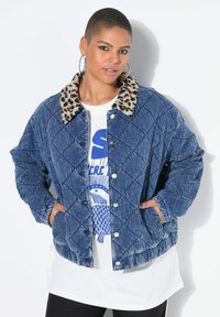 Kurtka dżinsowa pikowana z kołnierzem w panterkę, niebieskiego koloru, zapinana na zatrzaski. Nałożona na białą koszulkę z nadrukiem.