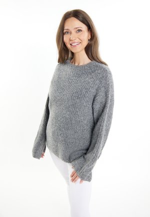 Pulover tricotat gri cu un finisaj texturat, mâneci largi și decolteu rotund, purtat peste pantaloni albi. Material moale cu o croială lejeră.