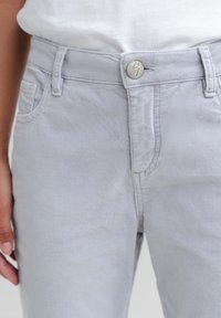 Svetle šedé denimové kalhoty s předními kapsami, kovovým zapínáním na knoflík a jemnými švy podél pasu.