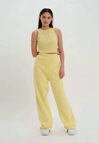 Crop top en maille jaune à encolure ronde, associé à un pantalon de survêtement jaune ample. La tenue présente un tissu texturé et des accents blancs.