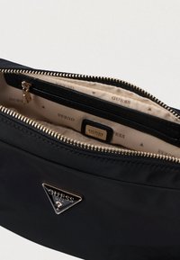 Μαύρη νάιλον τσάντα clutch με χρυσές λεπτομέρειες, κλείσιμο με φερμουάρ και εσωτερικό σε μπεζ απόχρωση με επαναλαμβανόμενο μοτίβο λογότυπου.