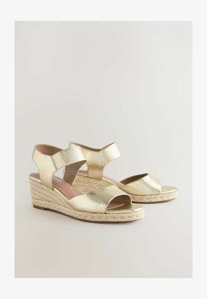 Guldfarvede metallic wedge sandaler med åben tå, crisscross stropdesign og vævet jute-bund. Har en glat tekstur og sikker ankelsupport.