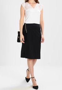 Vit topp med spets ärmklädsel, parat med en figurformad svart pennkjol. Svarta spetsiga klackar och en liten svart axelväska kompletterar outfiten.