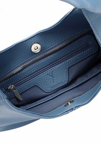 L'interno della borsa a tracolla blu in pelle presenta una tasca con zip, una chiusura a scatto e una fodera in tessuto morbido. Include dettagli in pelle testurizzata.