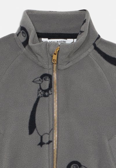 Grå fleecejakke med gullglidelås, med et svart pingvinmønster og høy krage. Myk tekstur, uformell design.