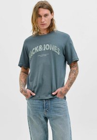 Pilkas medvilnės marškinėlis su dideliais, tekstūriniais žodžiais "JACK&JONES", derinamas su šviesiai mėlynomis džinsinėmis kelnėmis. Laiduotas kirpimas ir apvalios iškirptės dizainas.