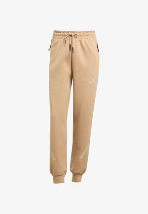 Beige sweatpants lavet af blødt materiale, med elastisk talje med snøre, sidelommer med lynlås og reflekterende detaljer.