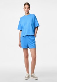 Tricou din bumbac albastru cu mâneci scurte, asortat cu șorturi albastre. Design confortabil, cu talie elastică și șnur de ajustare. Adidași casual.
