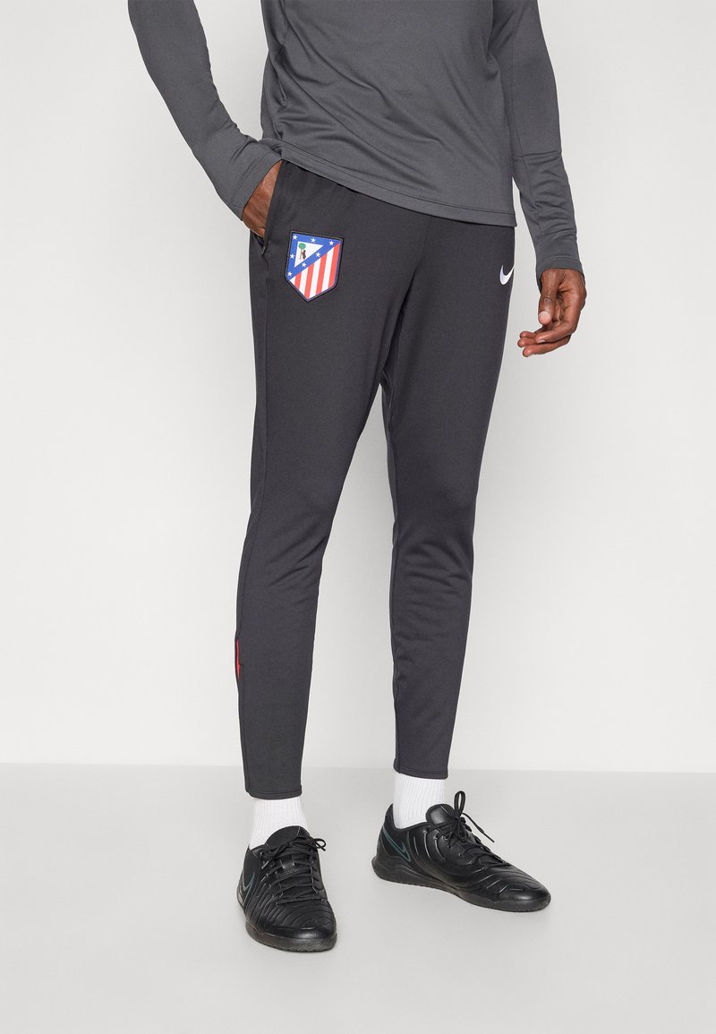Pantalons de sport gris avec une coupe ajustée, arborant un logo de club bleu et rouge sur la cuisse gauche et un petit accent rouge sur la taille.