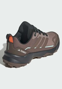 Smeđe i crne Adidas Terrex trail tenisice s narančastim jezikom, mrežastim gornjim dijelom, odsjajnim detaljima i robusnim potplatom za vanjsku upotrebu.
