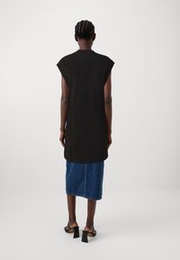 Černá bezrukává pletená tunika s žebrovanými okraji, spárovaná s modrou džínovou sukní. Černé sandály s blokovým podpatkem doplňují vzhled.