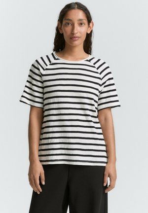 T-shirt à manches courtes rayé noir et blanc avec un col rond et des manches raglan, fabriqué en tissu doux. Porté avec un pantalon large noir.