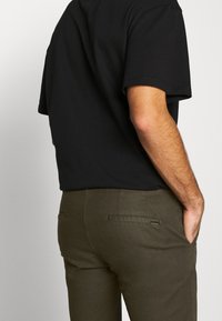 Czarny krótki T-shirt z krótkim rękawem w połączeniu z oliwkowozielonymi spodniami z tylnymi kieszeniami i gładką fakturą.