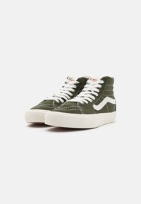 Un paio di sneakers alte verdi con lacci bianchi, suole in gomma bianca e una striscia ondulata bianca sui lati, su uno sfondo bianco.