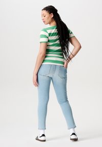 Groen en wit gestreept shirt met korte mouwen, lichtblauwe denimjeans en zwart-witte sneakers. Lange gevlochten haren, minimalistische stijl.