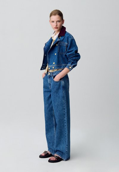 Chaqueta de denim con un cuello burdeos, herrajes dorados y pantalones de denim de pierna ancha. Tela texturizada, corte relajado y sandalias de punta abierta con hebilla.