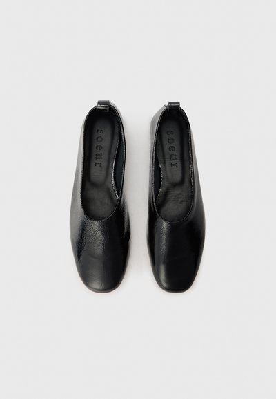 Chaussures noires en cuir à enfiler avec une finition lisse, des bouts ronds et une semelle plate. Équipées d'une petite boucle au talon pour un enfilage facile.