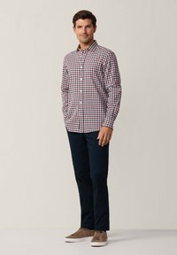 Camicia button-up scozzese in rosso, bianco e blu navy; maniche lunghe; vestibilità rilassata. Abbinata a pantaloni blu navy scuro e scarpe marroni chiare.