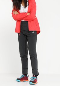 Veste légère rouge, t-shirt blanc, pantalon noir, baskets colorées avec des accents turquoise, conçues pour une utilisation active en extérieur.