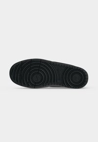 Suela de goma negra de un zapato Nike con patrones de dibujo circulares y logotipos de Nike en las zonas del talón y del antepié.
