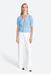 Cardigan lavorato a maglia blu chiaro con scollo a V, maniche a sbuffo corte, motivo in pizzo testurizzato e chiusura con bottoni frontale, abbinato a pantaloni bianchi a gamba larga.