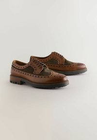Chaussures en cuir marron avec un panneau en tissu vert texturé, des détails brogue et une épaisse semelle en caoutchouc noir. Design à lacets, construction durable.