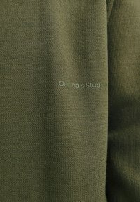 Suéter de punto verde oliva, con una textura suave y un sutil logotipo "Originals Studio" impreso en color a juego. Diseño minimalista.