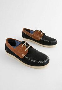 Scarpe in suede nere con un accento in pelle marrone, design con lacci, suola color crema e cuciture bianche. Texture morbida e stile casual.