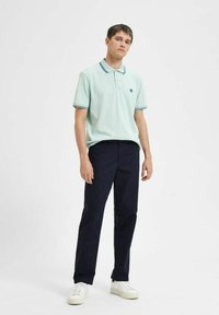 Polo shirt in light mint with contrast collar, paired with dark navy pants and white sneakers, offering a relaxed fit and clean lines.