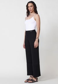 Pantalons larges à côtes noires avec taille haute, associés à un débardeur ajusté blanc et des sandales noires à lanières avec des accents argentés.