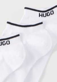 Kolm paari valgeid sokke, millel on must soonikserv ja "HUGO" logo tikkimisel musta värviga ülaosas. Valmistatud pehmest, tekstuurse materjalist.