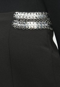 Δύο σειρές ασημένιων μεταλλικών δισκίων που είναι συνδεδεμένα οριζόντια γύρω από την μαύρη ύφασμα περιοχή της μέσης ενός ενδύματος.