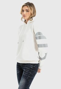 White hoodie with gray graphic stripes on sleeves, featuring a drawstring hood and ribbed cuffs, paired with dark denim jeans.