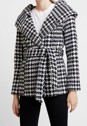 Abrigo de patrón de espiga en blanco y negro con un cuello oversized, cintura ceñida y mangas largas. Fabricado con tejido texturizado.