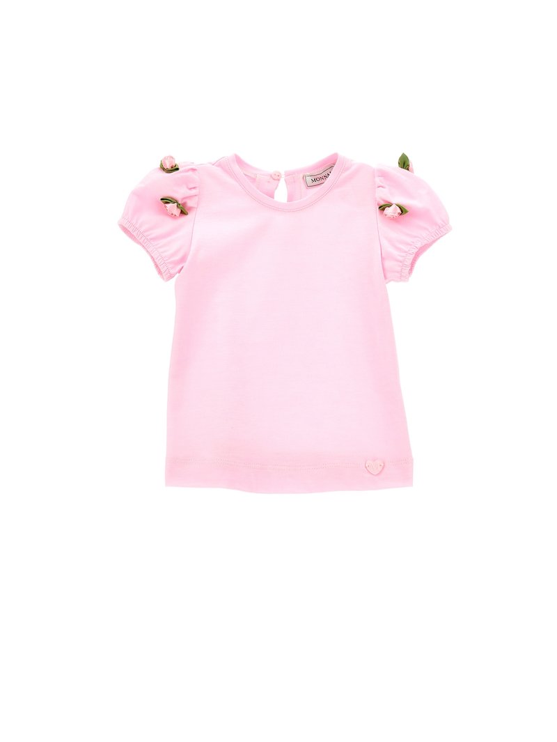 T-shirt di cotone rosa con maniche corte a sbuffo, con dettagli floreali e un logo a forma di cuore nella parte inferiore. Collo rotondo con chiusura a bottone.