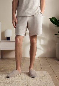 Light beige ribbed loungewear set, featuring a short-sleeve top and mid-length shorts. Accented with slip-on, textured slippers. Wood floor setting.