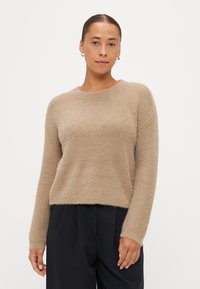 Beige kötött pulóver puha, texturált felülettel, kerek nyakkivágással és hosszú ujjakkal, sötét nadrággal párosítva.